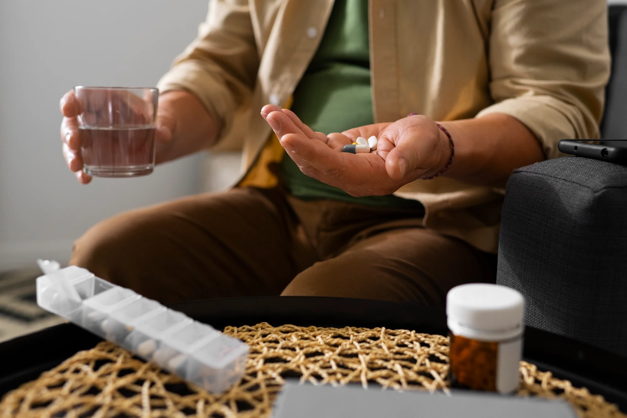 Person holding pills and a glass of water next to a pill organizer