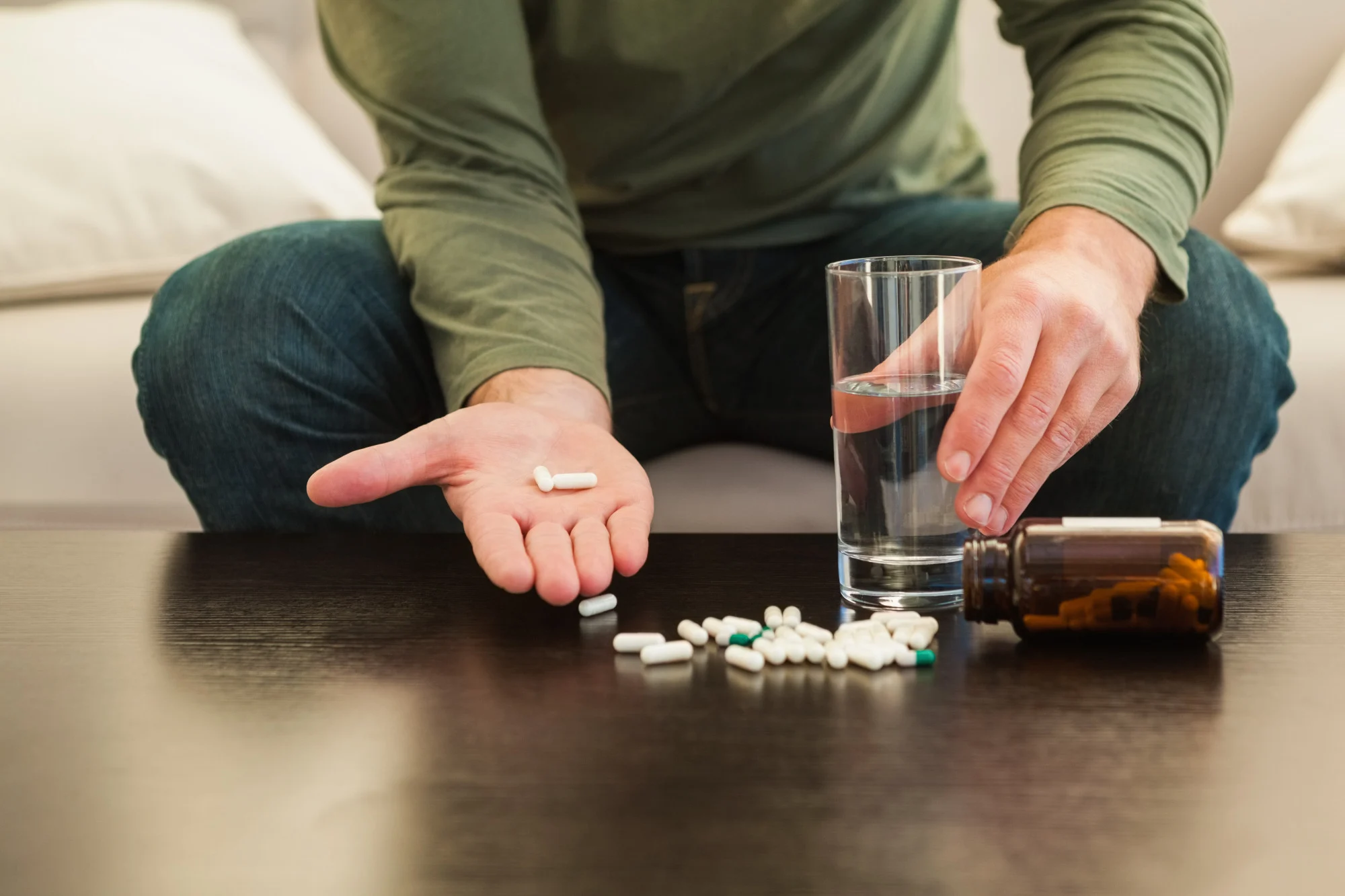 Man holding pills over a table with a glass of water