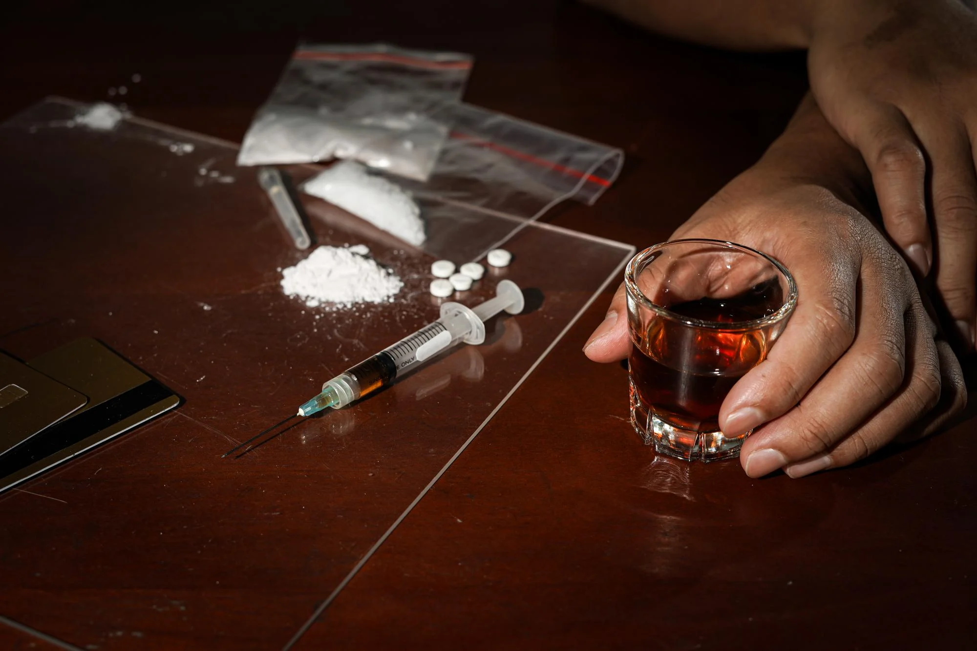 Substances, a syringe and a glass of alcohol on a dark table